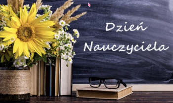Biały napis "Dzień Nauczyciela" na szkolnej tablicy. Przed tablicą stoją kwiaty i książki
