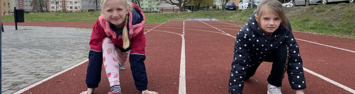 Dwie dziewczynki na bieżni na boisku przygotowują się do biegu